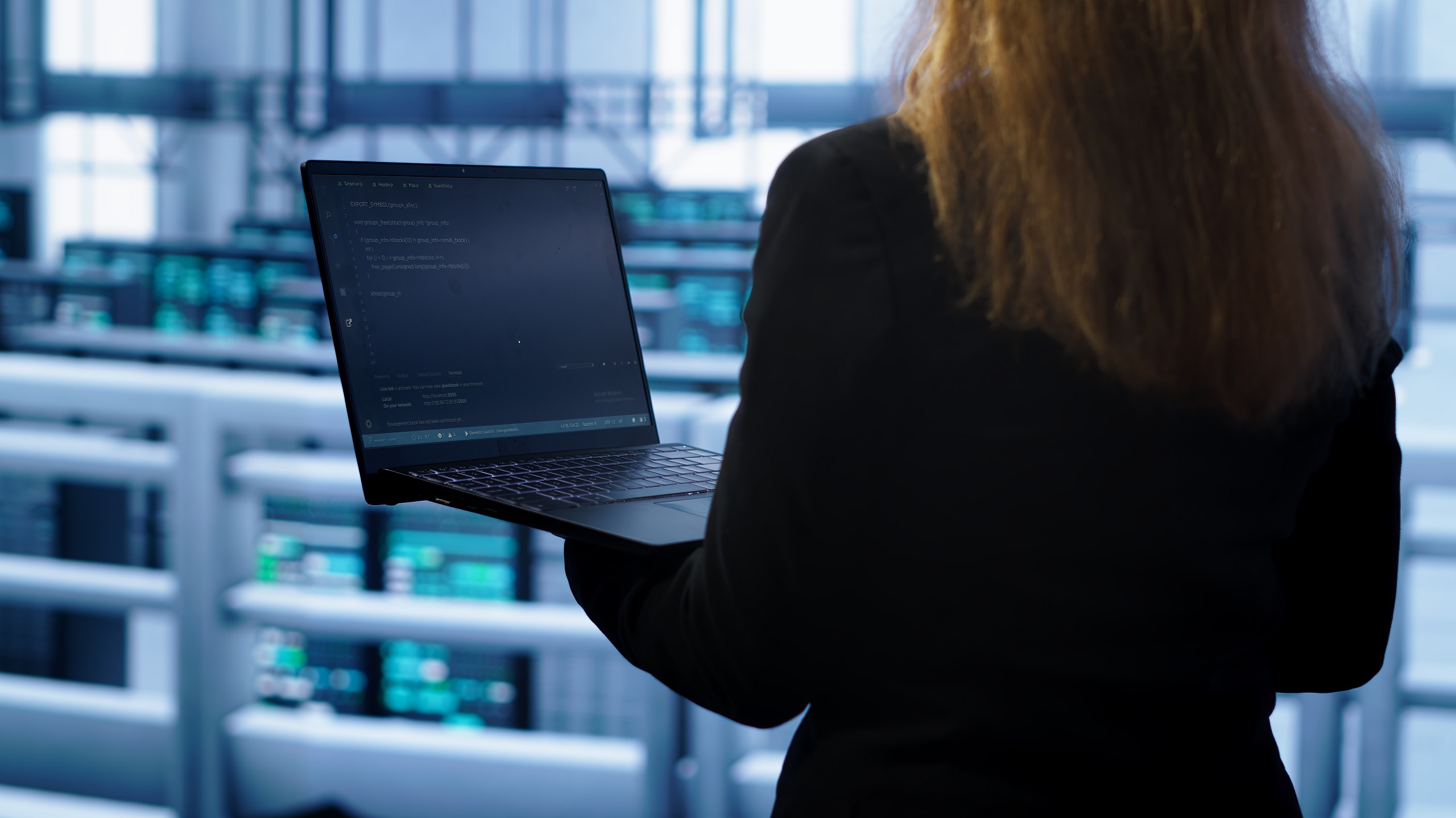 Person holding a laptop while monitoring systems inside a server environment.