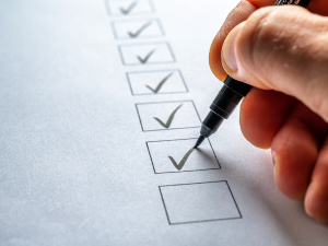 Hand using a pen to check off items on a printed checklist, representing a completed employee exit or security process.