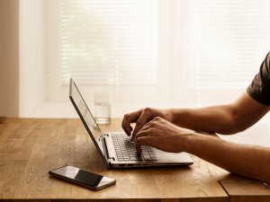 Person working on a laptop at a desk with a smartphone nearby.