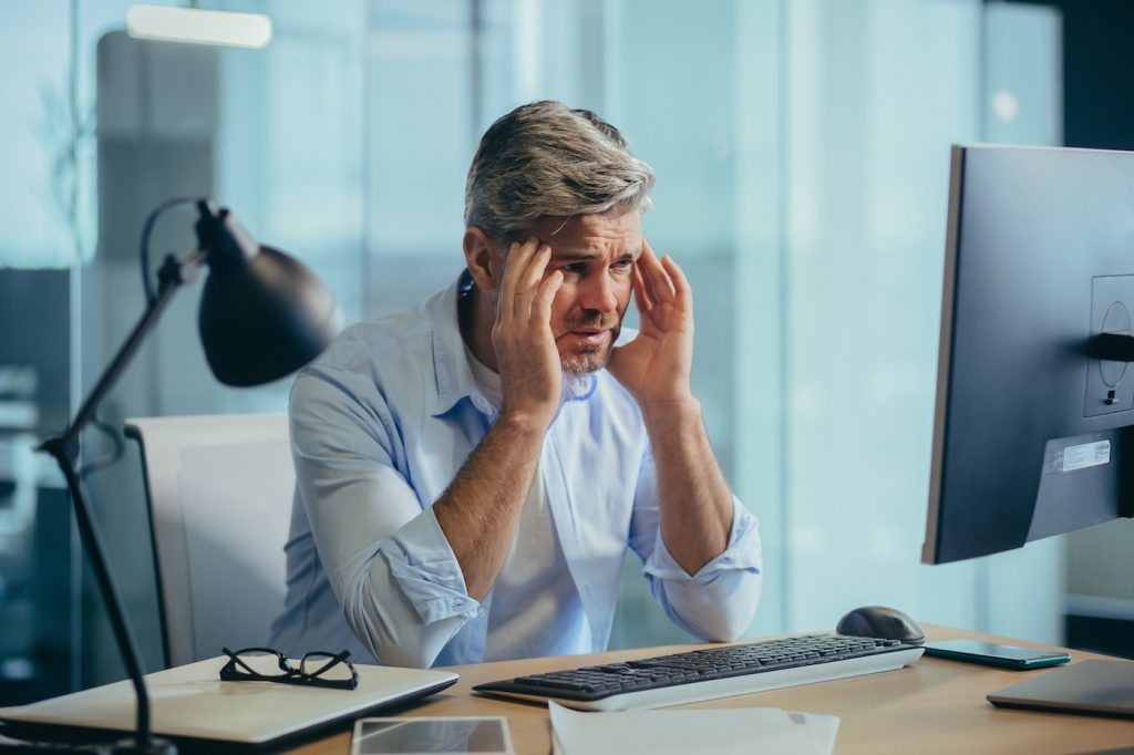  Business owner stressed at computer dealing with unexpected Windows software updates for business causing downtime.