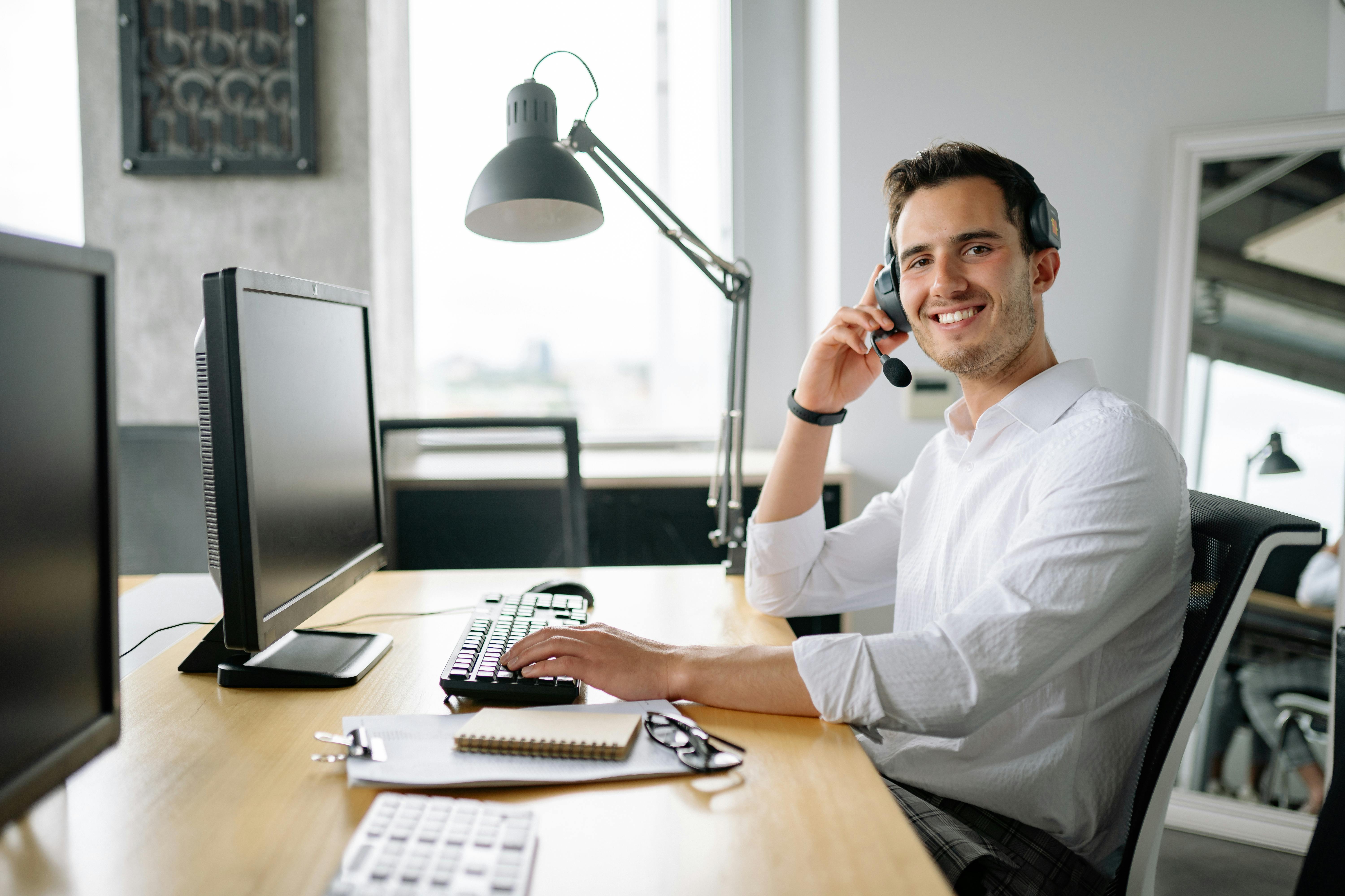 Smiling male support agent with headset typing at desk