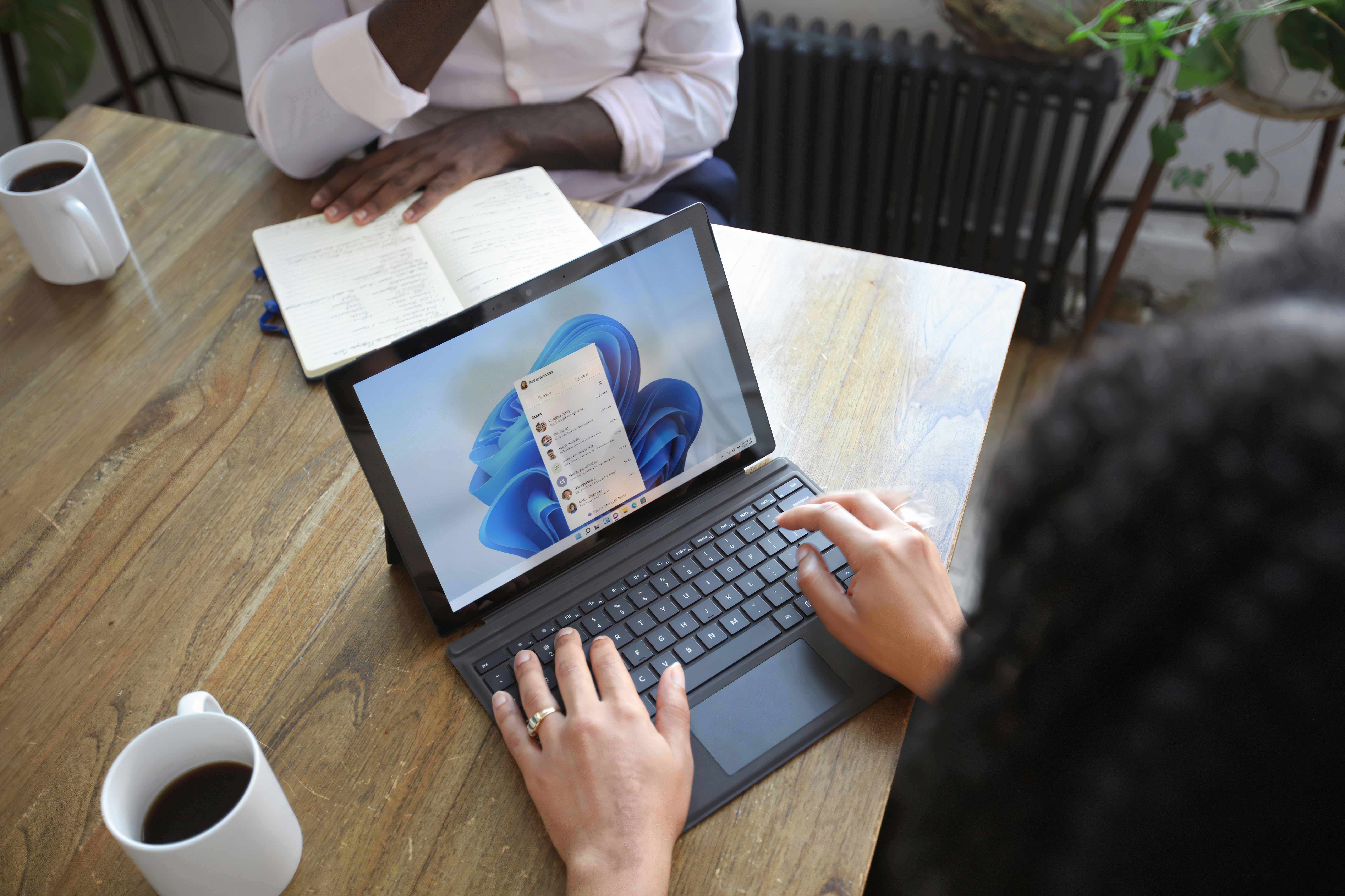 Person typing on Windows tablet with keyboard and coffee nearby