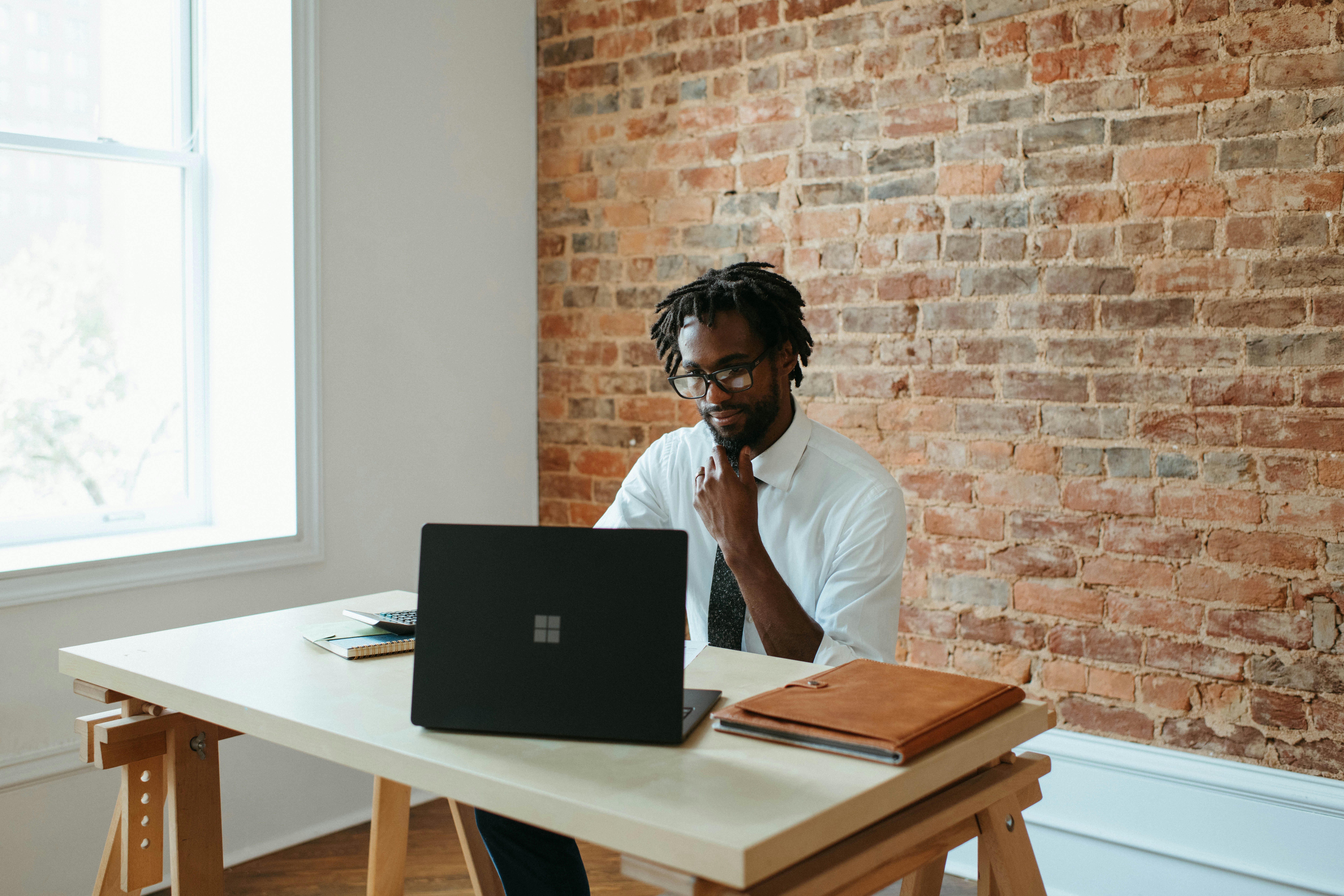 Man working on laptop at minimalist desk by brick wall