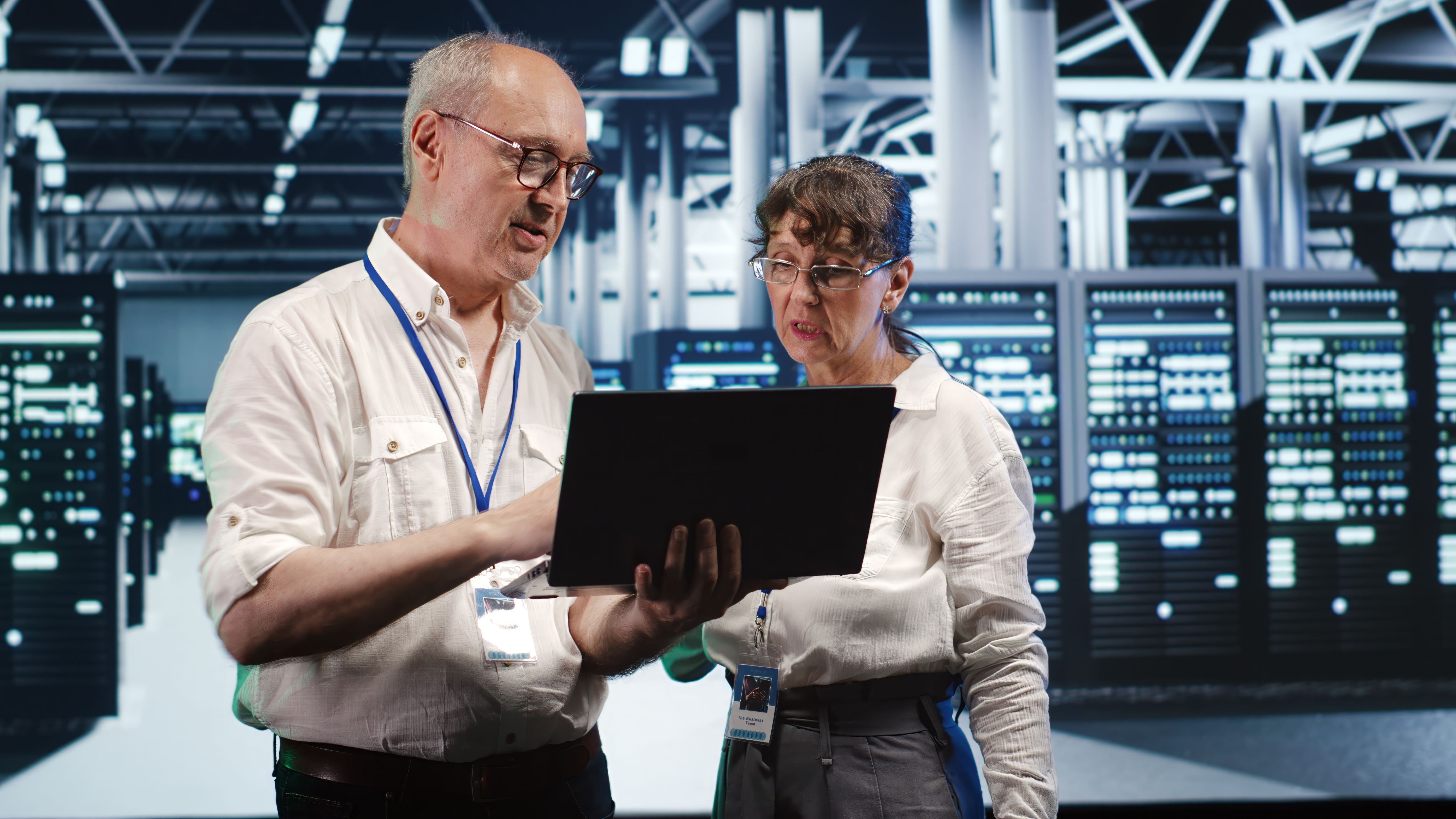 Two engineers having discussion while holding laptop inside data center.