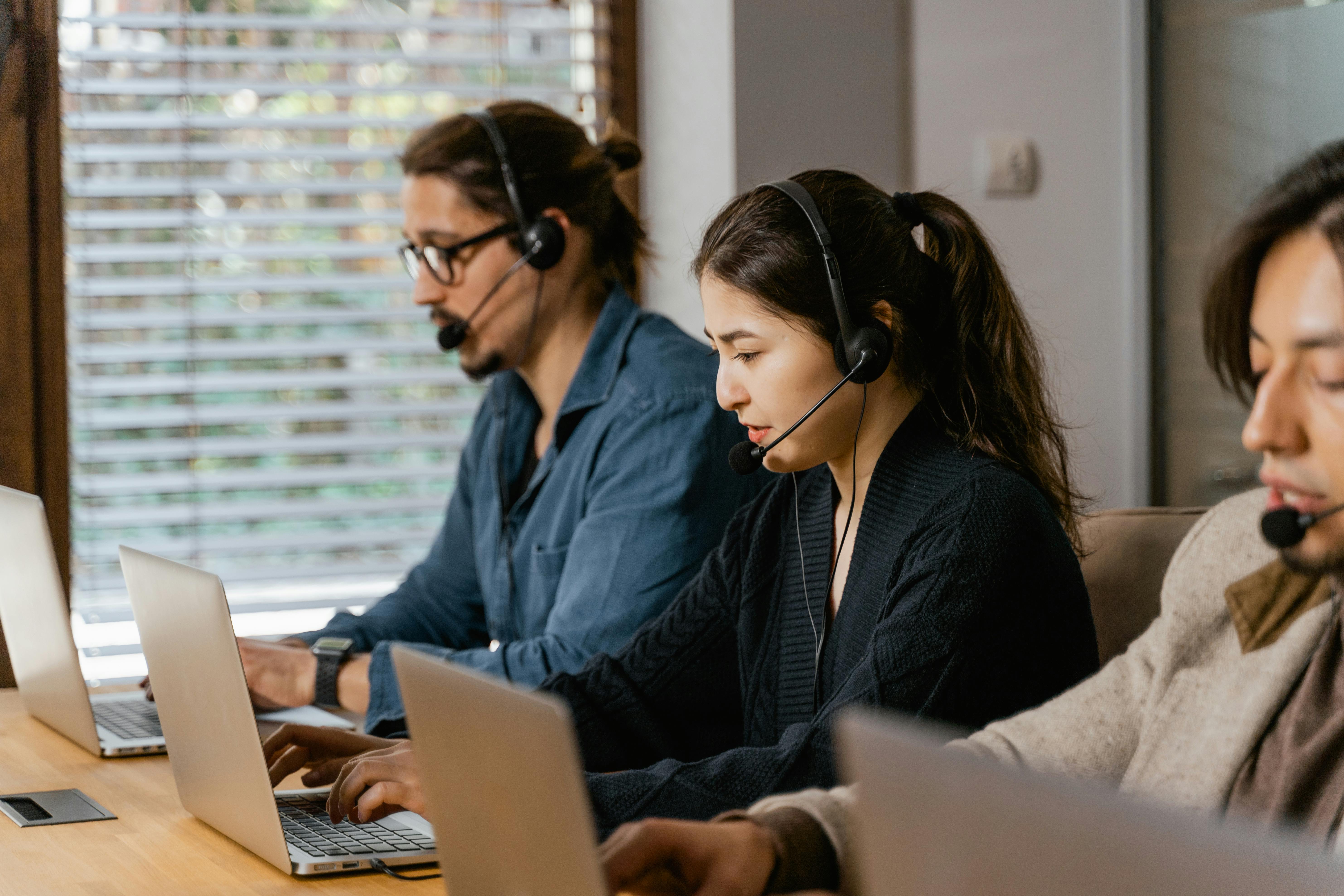 IT helpdesk professionals wearing headphones in front of laptops.