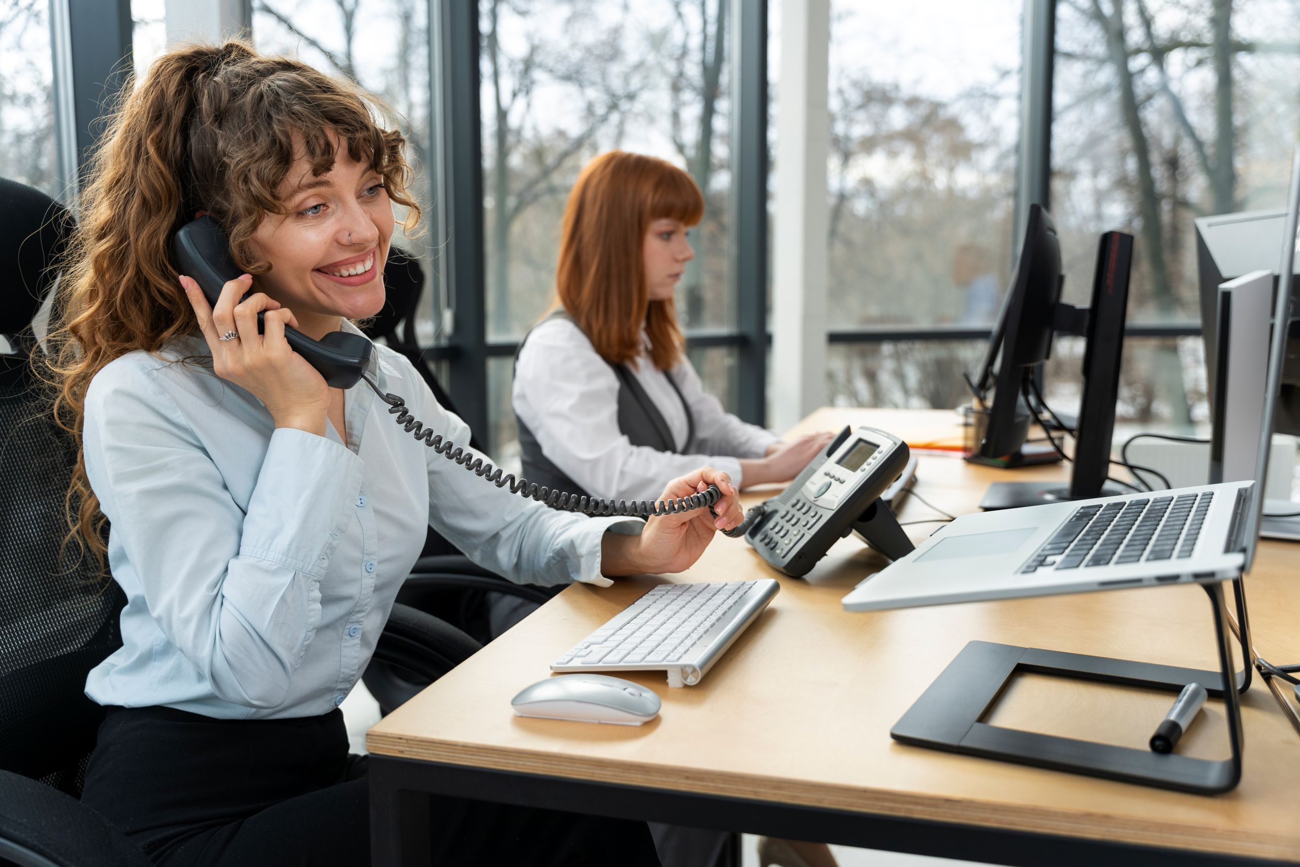 Woman answering phone in work station beside colleague.