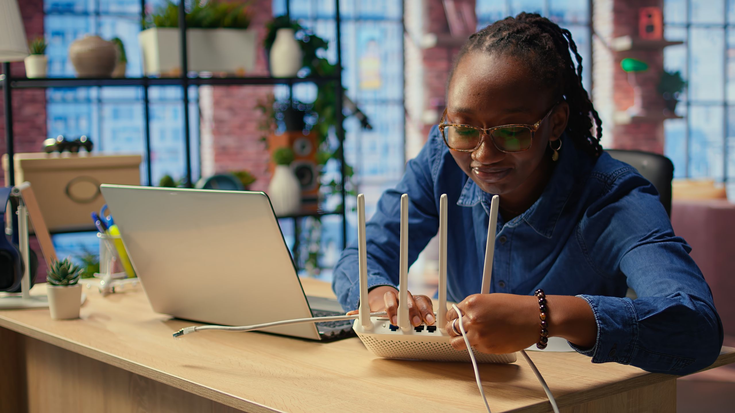 Woman connecting cables to a WiFi router in front of laptop.